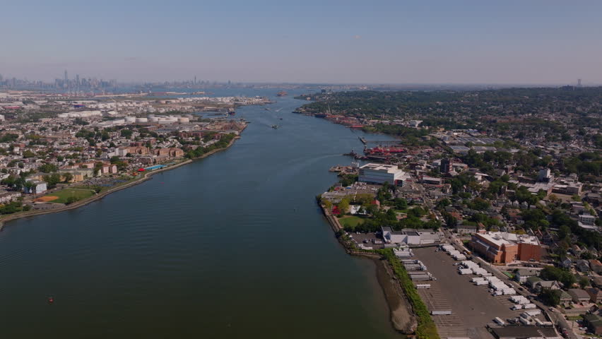 Drone aerial view of the Kill Van Kull waterway with Staten Island and Bayonne shorelines, industrial ports, and distant Manhattan skyline. Maritime shipping route on a clear sunny summer day. ProRes.