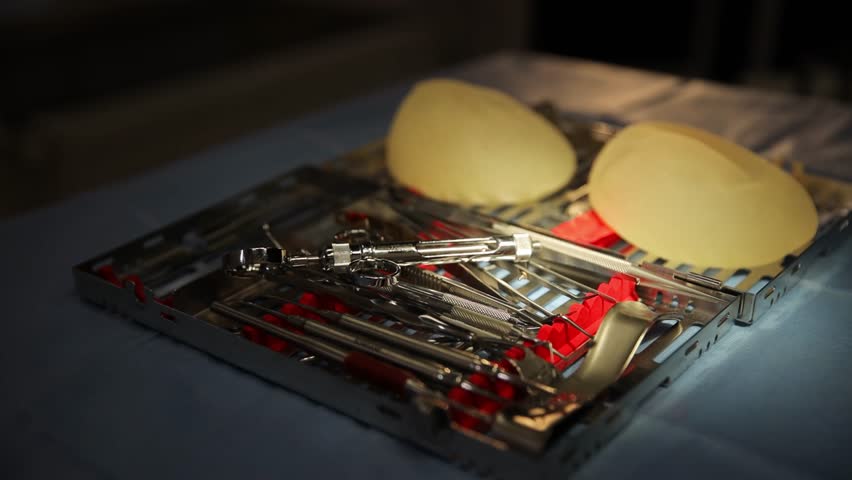 A carefully arranged collection of surgical instruments paired with breast implants on a sterile medical surface