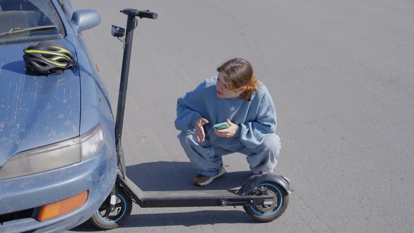 Woman examines and photographs the damage caused by a collision between an electric scooter and a car.