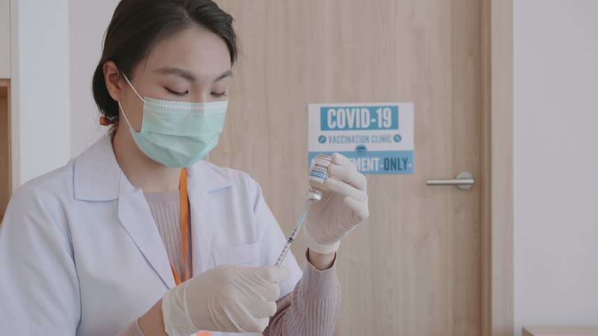 A healthcare worker wearing a mask and gloves prepares for a vaccination appointment in a clinic setting, ensuring safety during the COVID-19 pandemic. - Powered by Shutterstock - Get 15% off with code: PIKWIZARD15