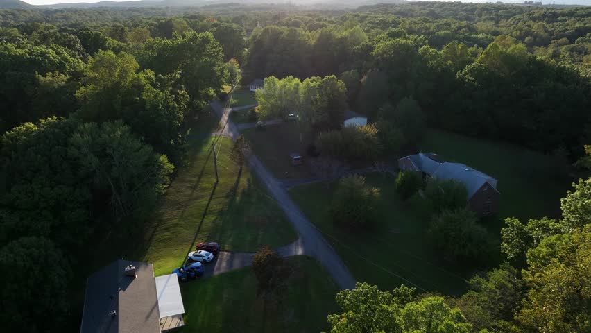 Peaceful charming housing area in green district of town. Sunset time in late summer. American rural neighborhood with parking cars on driveway. Aerial Birds Eye shot.