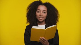 Smiling young woman in black blazer holding an open yellow book against bright yellow background, combining learning and creativity with positivity. - Powered by Shutterstock - Get 15% off with code: PIKWIZARD15