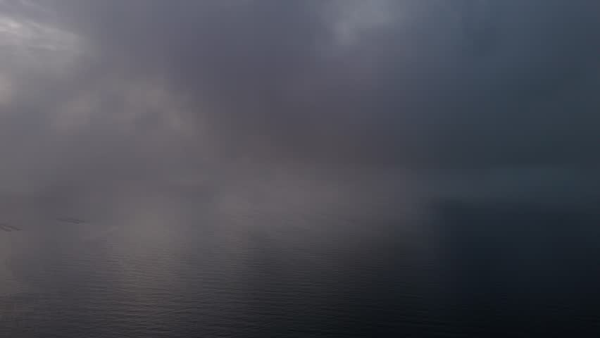 Low aerial flight through dense clouds at dawn showing sunlight casting orange and gold highlights on moving clouds.