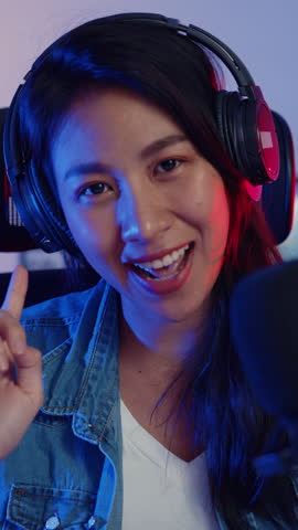 Vertical Screen : Happy asia girl blogger music influencer looking at camera broadcast record wear headphone online live talk microphone audience in living room home studio at night. Content creator.