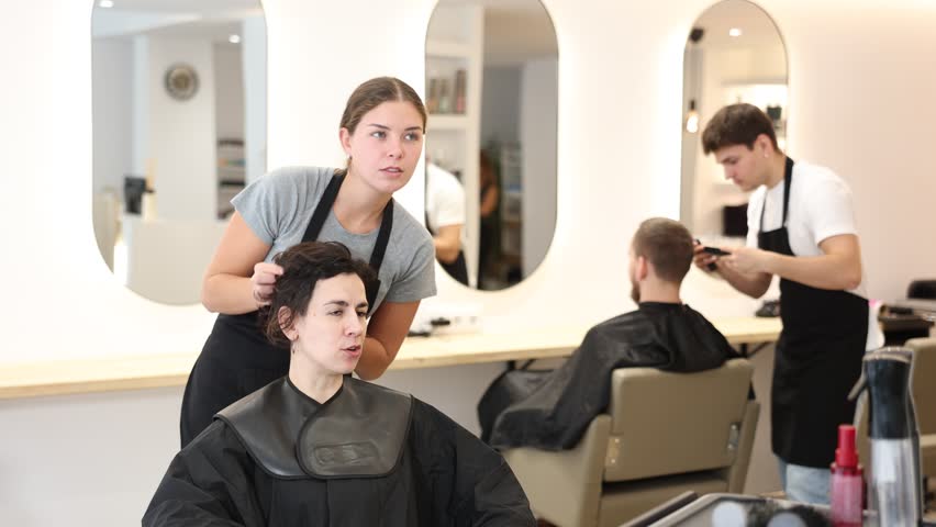 Female hairdresser stylist gives haircut to adult woman client in beauty salon 