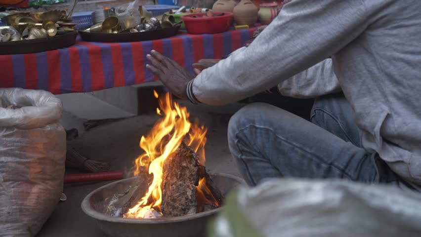 Mature village men warming hands in winter fire outside shop, Bihar, Northern India, handheld shot