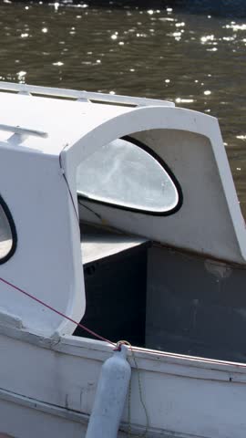White motorboat floats and gently drifts on sunlit loch, camera pans along hull exterior