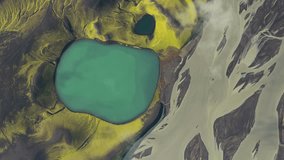 Aerial view of a lake's turquoise water contrasts sharply with the surrounding dark, mossy landscape, alongside a braided river, Fjallabak Nature Reserve, Rangárþing ytra, Iceland. - Powered by Shutterstock - Get 15% off with code: PIKWIZARD15