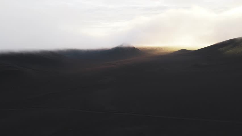 Aerial view of Landmannaleið, where the stark contrast between the dark volcanic landscape and the ethereal mist creates a dramatic scene, Fjallabak Nature Reserve, Rangárþing ytra, Iceland.