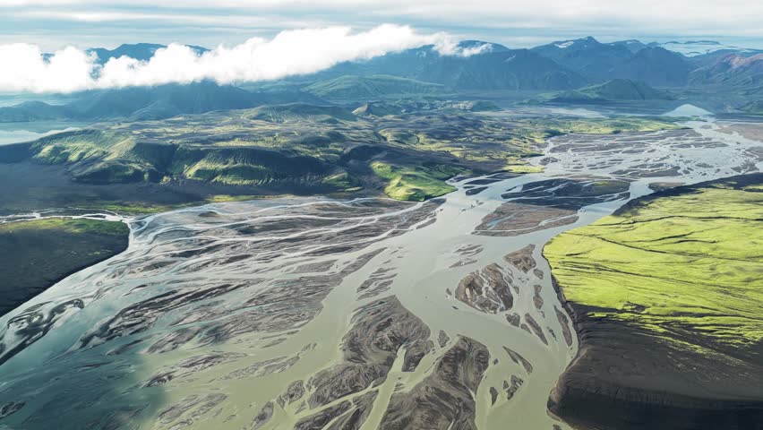 Aerial view of braided rivers carving through the landscape, contrasting stark grey riverbeds with vibrant green highlands, Landmannaleið, Rangárþing ytra, Iceland.