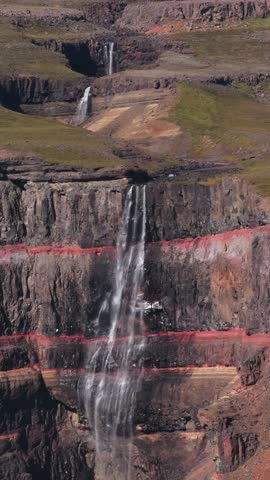 Aerial view of Hengifoss cascading down layered cliffs, contrasting dark rock with red clay, creating a stunning natural vista, Hengifoss, Fljótsdalshreppur, Iceland.