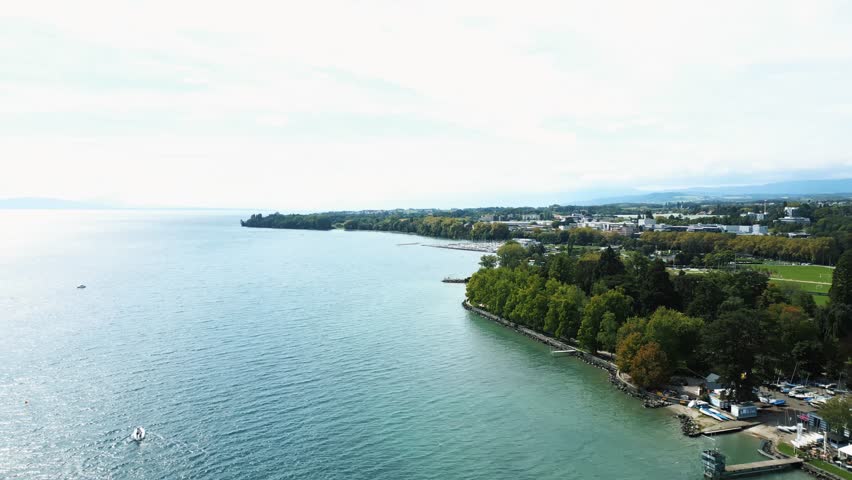 Aerial view of the shoreline, where turquoise waters meet lush green trees and buildings, creating a vibrant contrast of colors, Lake Geneva, Morges, Vaud, Switzerland.