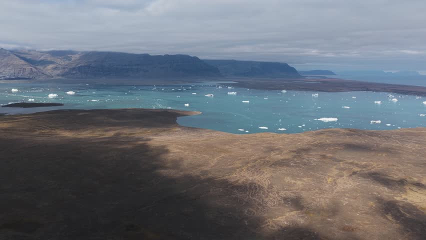 Aerial view of the glacial lagoon at Jökulsarlon, with scattered icebergs contrasting against the textured terrain, Jökulsarlon, Sveitarfélagið Hornafjörður, Iceland.