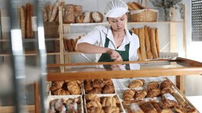 Woman seller stands at bakery counter with basket filled with fresh croissants. Employee puts croissants in window, arranges display of goods, complements assortment, puts buns on sale  - Powered by Shutterstock - Get 15% off with code: PIKWIZARD15