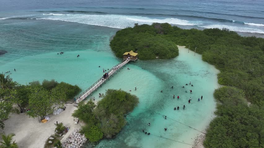Aerial view of a verdant island fringed by turquoise waters meeting the deep blue sea, and Maldivian people enjoying themselves in the lagoon, Thulusdhoo, North Male Atoll, Maldives.