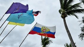 Strong Wind Blowing Palm Trees and Flags, Thailand Royal Family Banners in Yellow, Blue, Purple, National Thai Flag, Russian Flag with Emblem and Large Cyrillic Inscription. Cloudy Sky Tropical Storm. - Powered by Shutterstock - Get 15% off with code: PIKWIZARD15