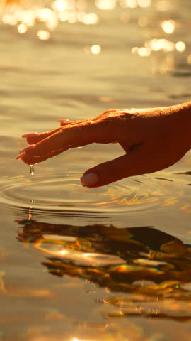 Hand Water Golden. Woman's hand drips water, forming ripples on calm surface during a radiant sunset.