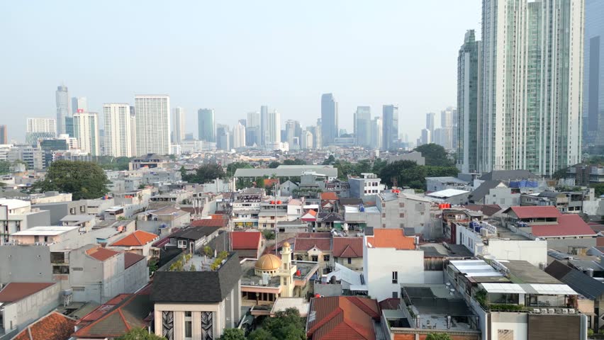 Aerial view of Jakarta city skyline with skyscrapers rising above traditional houses. Contrast of modern architecture and dense low-rise residential area in Indonesia