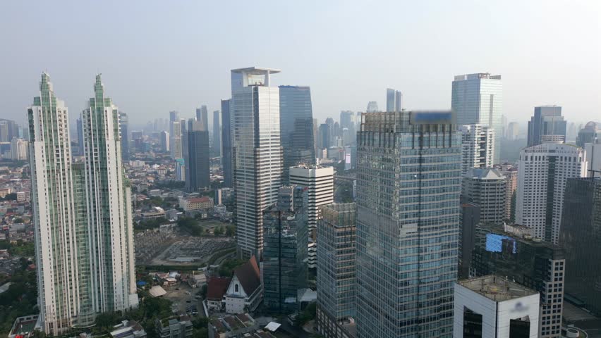 Cinematic aerial view of Jakarta city skyline with tall skyscrapers and modern office buildings in the business district. Urban landscape of Indonesia on sunny day.