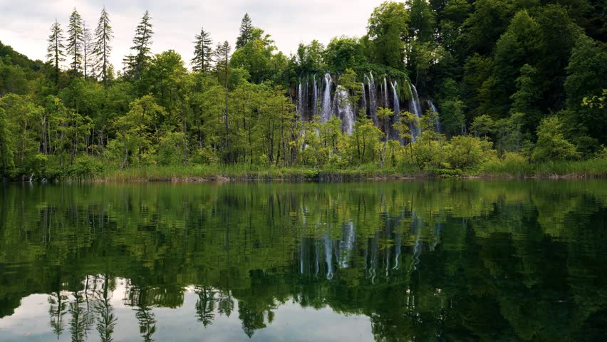 Emerald lakes of Plitvice Croatia reflecting forest, waterfall and sky in UNESCO heritage landscape