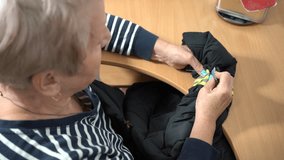Sew a reflector on sleeve of a black jacket. Grandma sews by hand with a thread and a needle. An elderly woman repairs clothes. Sewing needlework by old hands - Powered by Shutterstock - Get 15% off with code: PIKWIZARD15