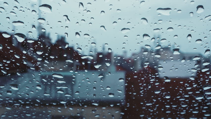 Raindrops on glass window with blurred cityscape of european buldings. Moody urban scene with soft focus, rainy weather, historical architecture