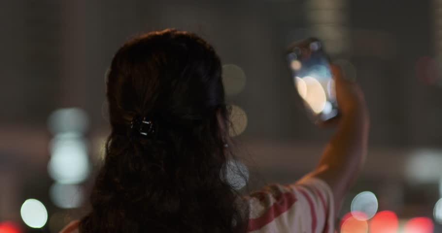 Tourist woman capturing photographs of Museum of the Future at night with Dubai highway traffic and illuminated skyscrapers