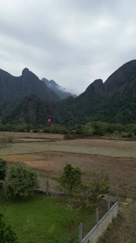 Aerial vertical drone view of Laos with mountains in the background, lush green landscape, tropical scenery under sunny sky, perfect Instagram and social media travel video.
