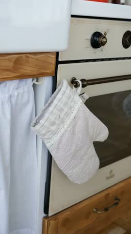 Kitchen oven mitt hangs from handle near oven door and white fabric curtain