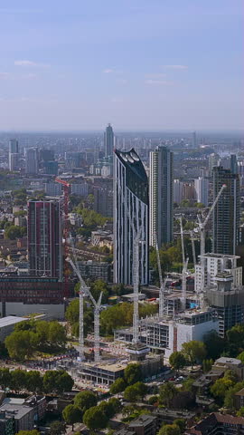 Vertical 4K drone video modern city skyline with iconic angular towers above green urban forest. Stunning aerial footage of architectural diversity and sustainable development for mobile video content
