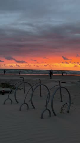 Sunset view over the Baltic Sea in Liepaja, Latvia. The orange sun is partially above the horizon, casting a warm glow across the sky and reflecting on the gentle waves. Tranquility and natural beauty