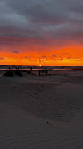 Sunset view over the Baltic Sea in Liepaja, Latvia. The orange sun is partially above the horizon, casting a warm glow across the sky and reflecting on the gentle waves. Tranquility and natural beauty