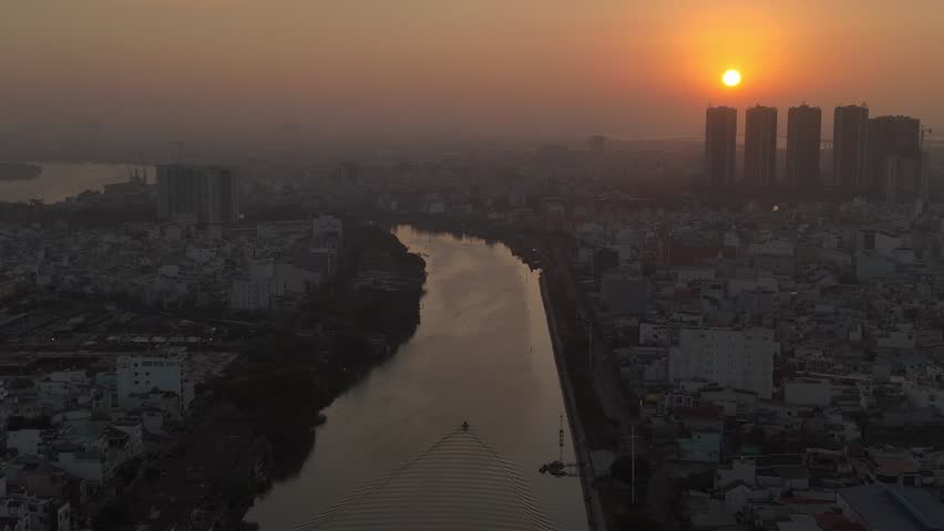 A series of drone clips capturing the winding Saigon River as it flows through the dense urban landscape of Ho Chi Minh City, Vietnam, at sunrise. The footage showcases the city's unique blend of natu