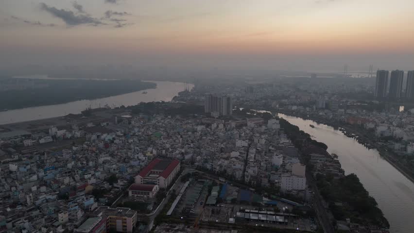 A series of drone clips capturing the winding Saigon River as it flows through the dense urban landscape of Ho Chi Minh City, Vietnam, at sunrise. The footage showcases the city's unique blend of natu