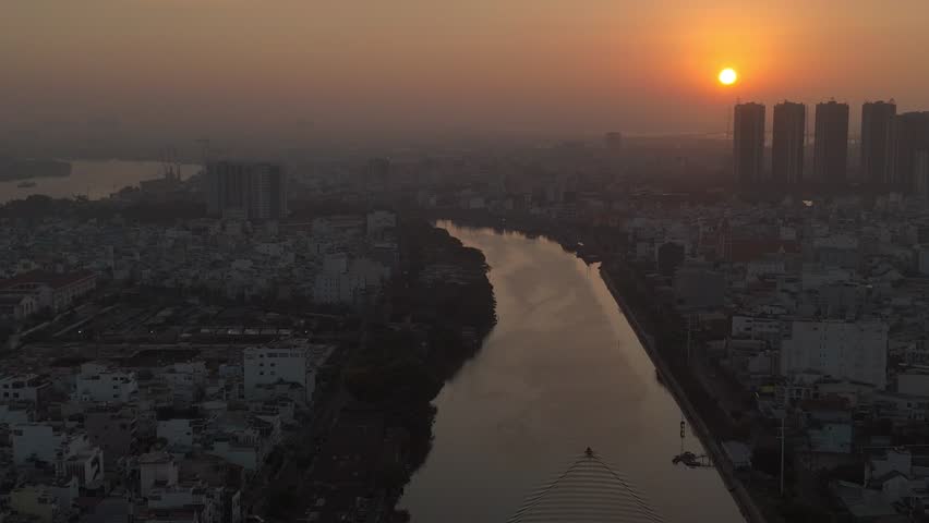 A series of drone clips capturing the winding Saigon River as it flows through the dense urban landscape of Ho Chi Minh City, Vietnam, at sunrise. The footage showcases the city's unique blend of natu