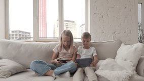 Children sitting on a sofa using digital devices, a boy with a tablet and a girl with a smartphone. Siblings together indoors, focused on technology, modern lifestyle scene - Powered by Shutterstock - Get 15% off with code: PIKWIZARD15
