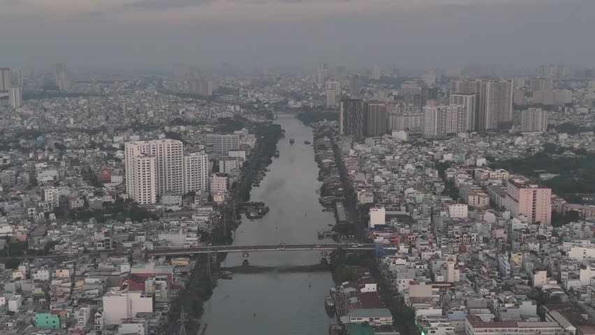 A series of drone clips capturing the winding Saigon River as it flows through the dense urban landscape of Ho Chi Minh City, Vietnam, at sunrise. The footage showcases the city's unique blend of natu