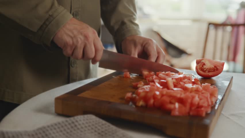 Fresh chopped tomatoes on wooden board, mans hands holding knife. Scene about mindful cooking ritual, calm preparation, and balance in everyday kitchen life. High quality 4k footage
