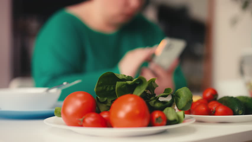 Close-up of fresh vegetables, woman using dieting app on phone on background