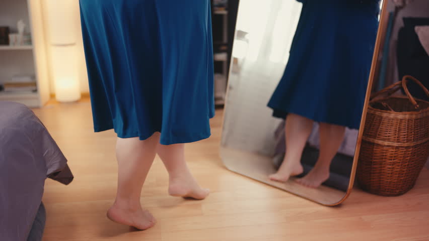 Feet of a plus size woman in blue dress posing near mirror with confidence