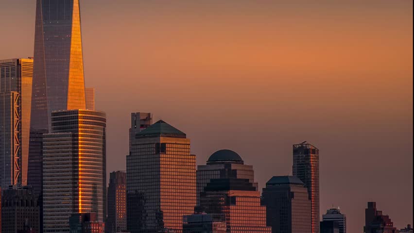 Aerial view of skyscrapers in Lower Manhattan, bathed in the warm glow of the setting sun, creating striking contrasts of light and shadow, New York, New York, United States.