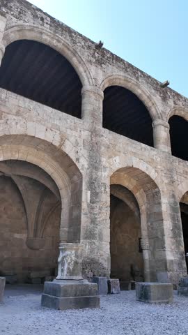 Medieval stone architecture inside the Palace of the Grand Master of the Knights in Rhodes, Greece. Historic arches and fortress walls under a clear blue sky.
