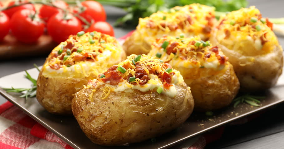 Woman adding bacon onto tasty stuffed baked potatoes at table, closeup