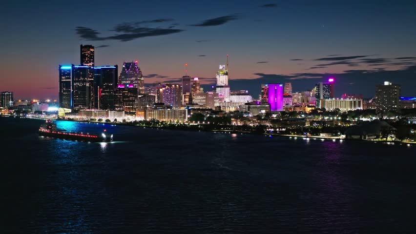 The detroit skyline glows with vibrant lights at night over the dark river