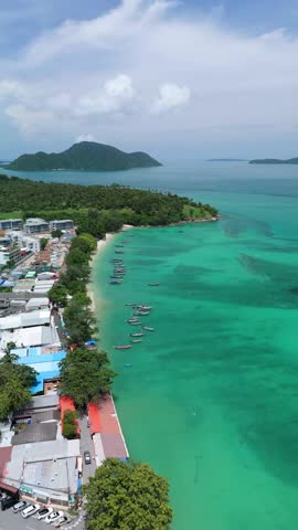 Drone descends flying over moored longtail boats along turquoise Rawai Beach
