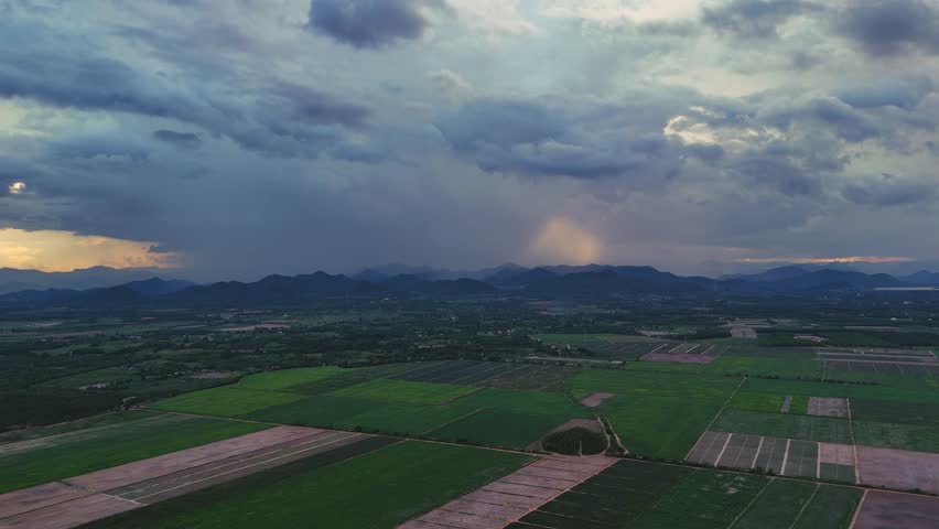 Aerial landscape of dark clouds and rain falling over mountains and agricultural fields