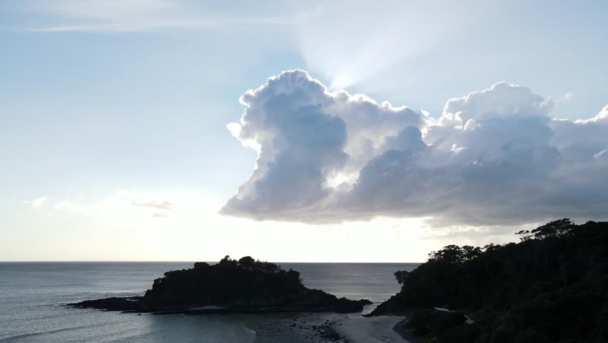 Dramatic shadow cast by a cloud across the scenic coastal headland, with the sun's rays being blocked as they emerge from behind the cloud. Aerial view