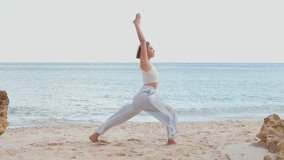 Young woman practicing yoga Warrior Pose on sandy beach stretching arms with ocean and serene natural backdrop focusing on balance, strength and mindfulness - Powered by Shutterstock - Get 15% off with code: PIKWIZARD15