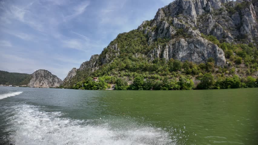 Danube river flowing through the Iron Gates gorge, with steep rocky mountains covered in green vegetation rising from the water, creating a dramatic natural landscape between Serbia and Romania