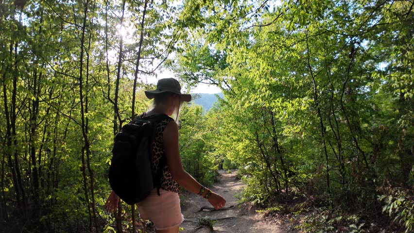 Hiker with backpack walking a forest trail in the Danube gorge, enjoying the sunlit nature and views over the Great Boilers area in Serbia and Romania. SLOW MOTION